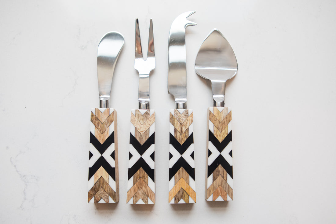 Set of four cheese knives with decorative wooden handles on a light gray background