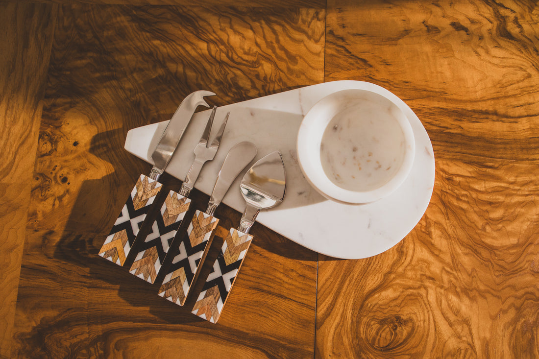 Set of knives, forks, and spoons in a decorative sheath on a marble plate with a wood surface background.