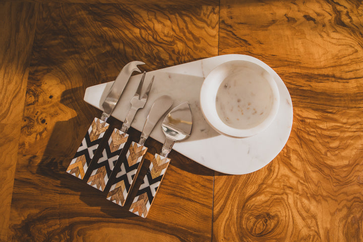 Set of knives, forks, and spoons in a decorative sheath on a marble plate with a wood surface background.
