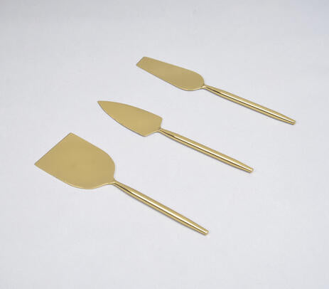 A set of three gold-colored stainless steel cheese serving utensils, including a cheese knife, a cheese spreader, and a cheese wedge server, displayed against a white background.