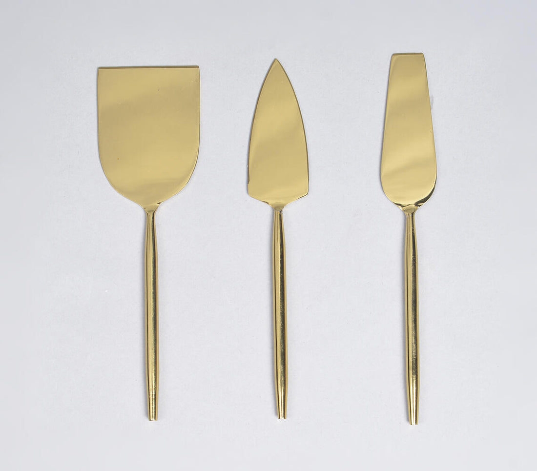 A set of three gold-colored stainless steel cheese serving utensils, including a cheese knife, a cheese spreader, and a cheese wedge server, displayed against a white background.