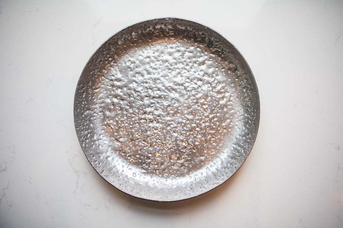 Silver decorative plate with a textured surface on a light gray background