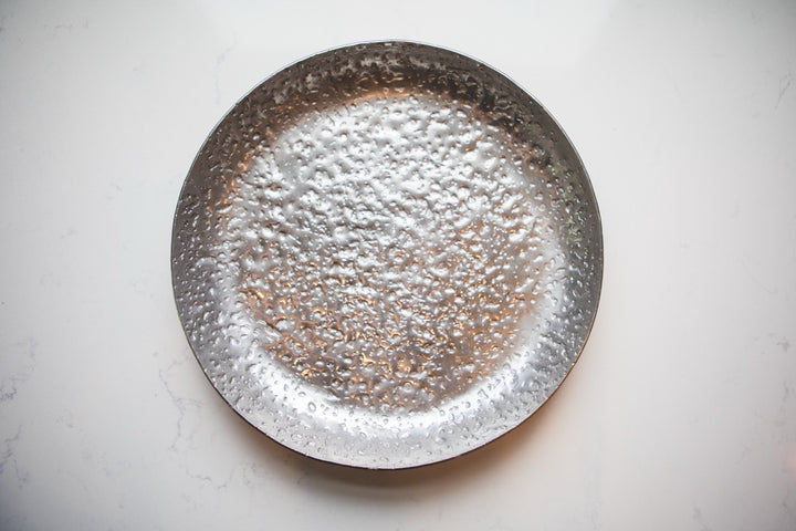 Silver decorative plate with a textured surface on a light gray background
