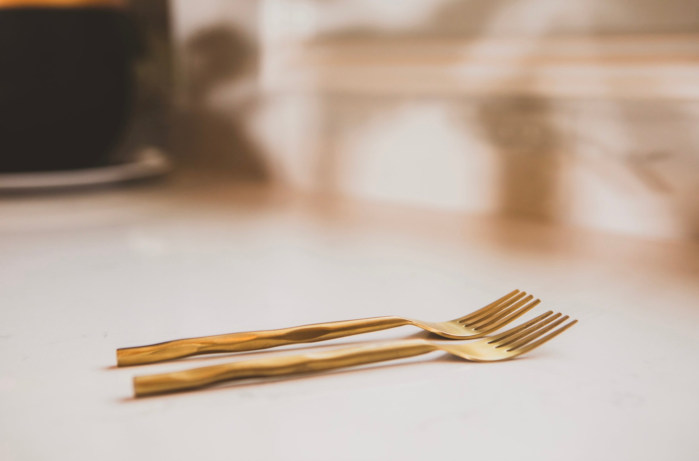 Two gold forks on a light surface with a blurred background