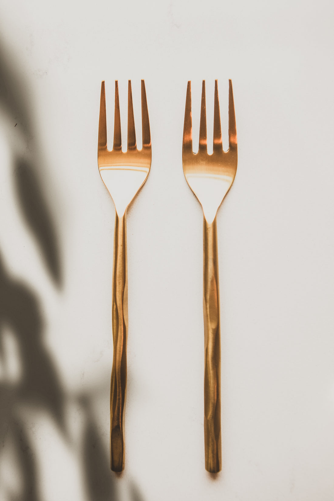 Two rose gold forks on a light background