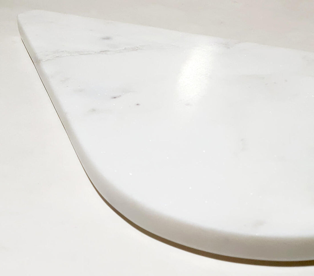 Close-up of a white marble cheese board with a smooth surface and curved edge.